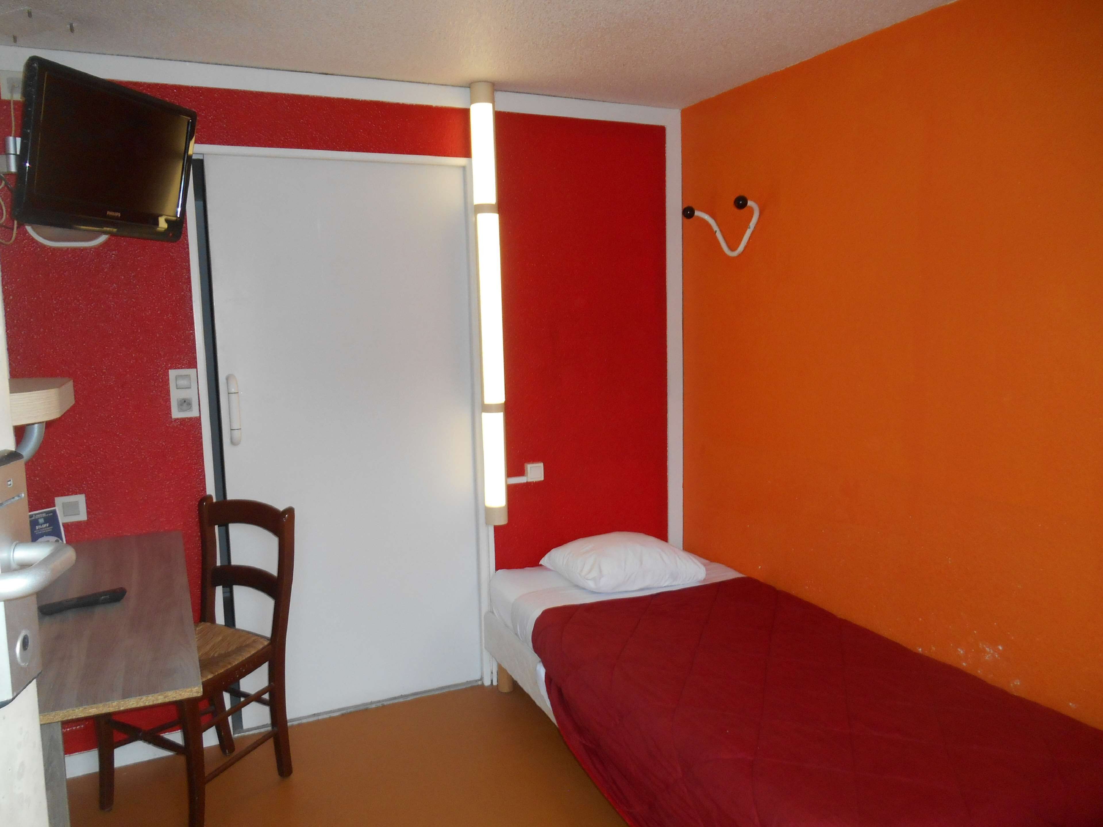Una habitación pequeña con una cama, una silla, un escritorio y un televisor.