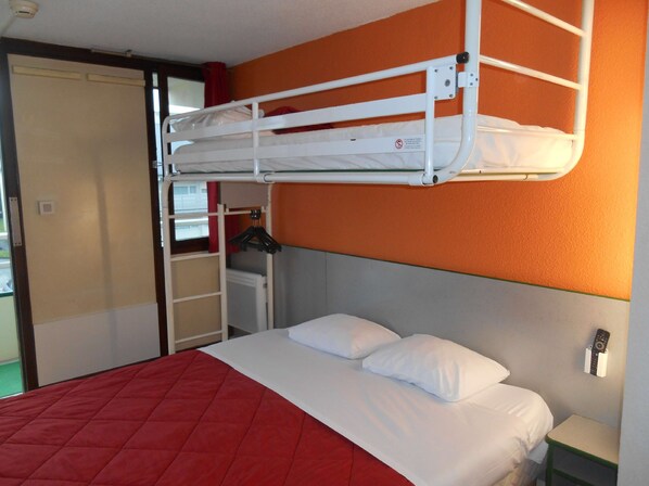Una cama litera con un edredón acolchado rojo, un colchón blanco y una almohada blanca. Hay una mesita de noche pequeña con un control remoto encima.
