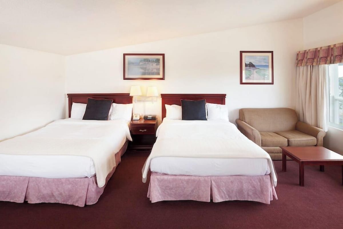 A hotel room with two beds, a sofa, a small table, and two framed pictures on the wall.