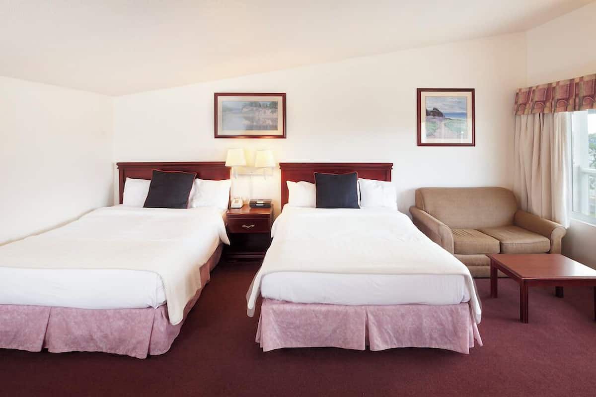 Une chambre d’hôtel avec deux lits, un canapé, une petite table et deux tableaux encadrés au mur.