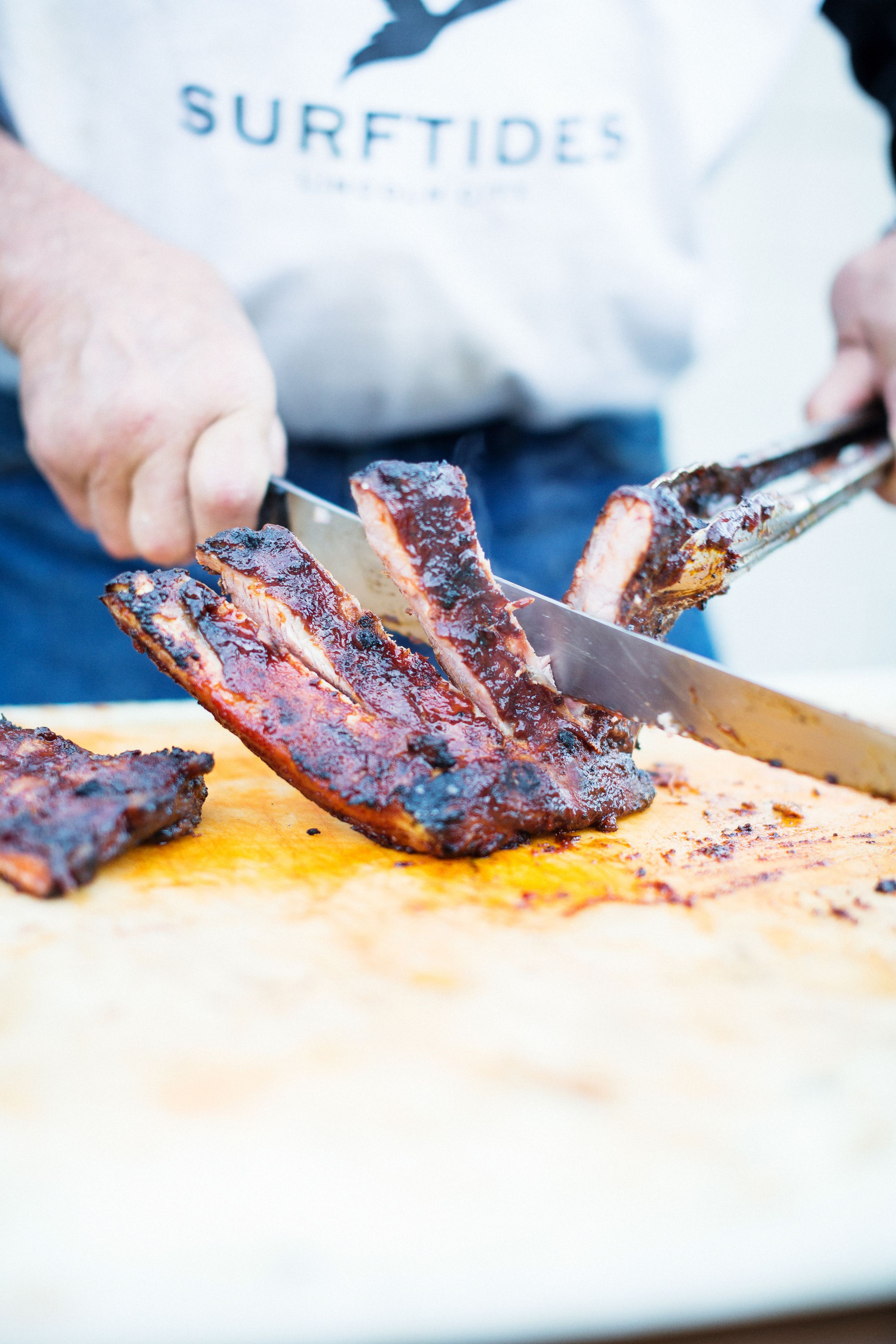 A person slicing grilled ribs on a cutting board.