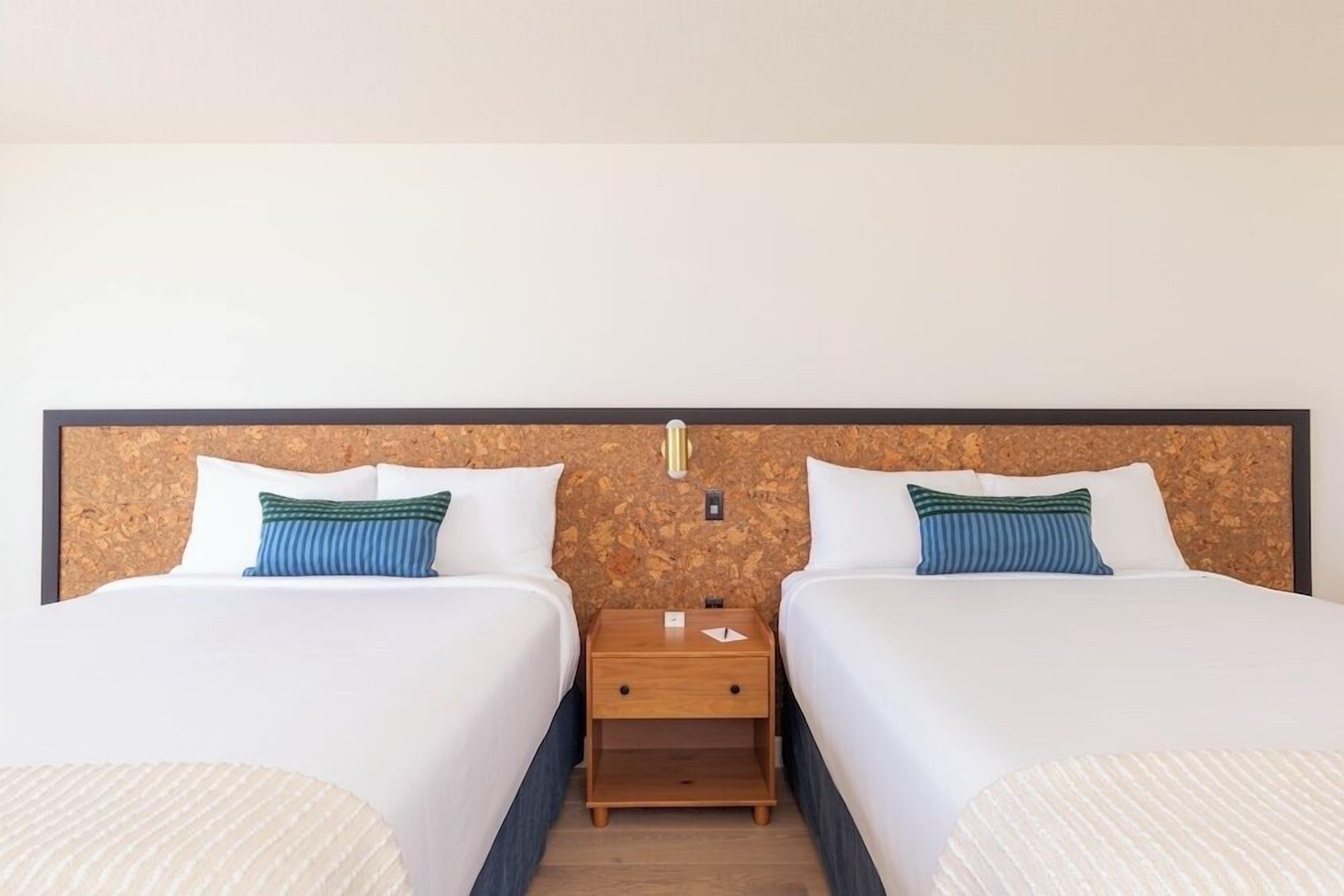Ein Hotelzimmer mit zwei Betten, einem hölzernen Kopfteil und einem Nachttisch dazwischen.