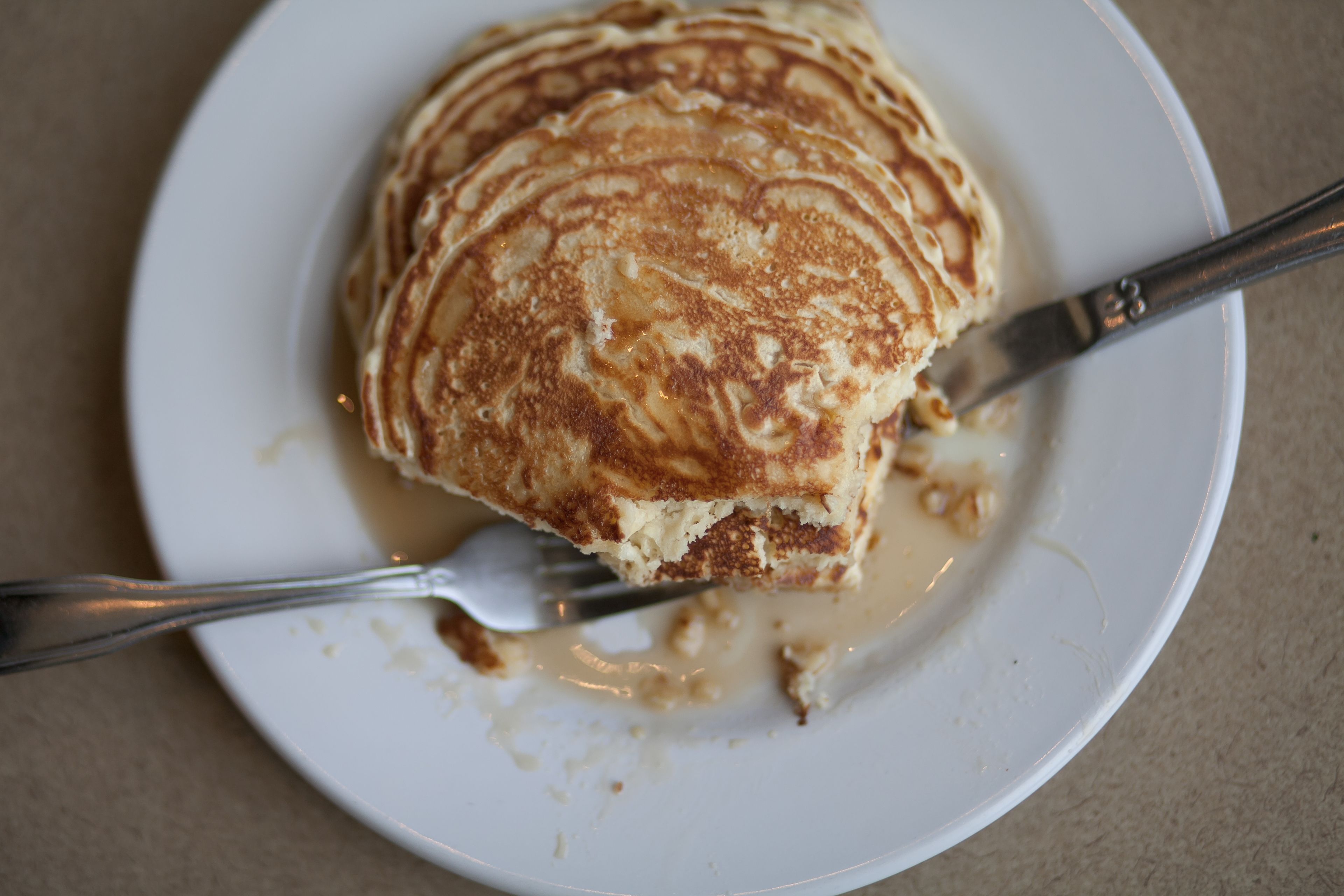 Una pila de tortitas en un plato blanco, con jarabe y un tenedor.