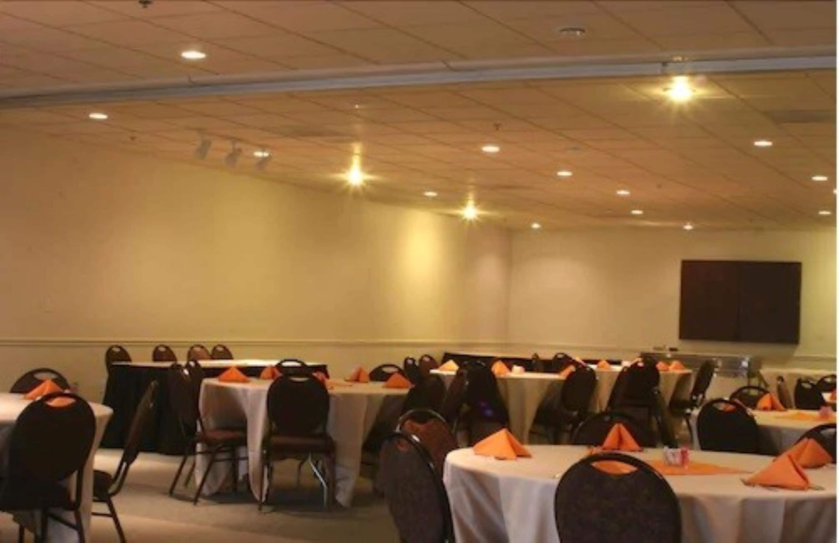 A conference room with tables set for meetings, equipped with chairs and tables, and a projector screen on the wall.