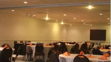 A conference room with tables set for meetings, equipped with chairs and tables, and a projector screen on the wall.