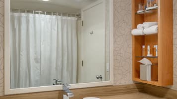 A bathroom with a large mirror, a wooden vanity, a white sink, and a shelf with toiletries.