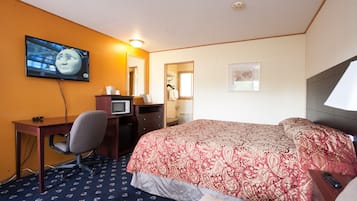 A hotel room with a bed, a desk with a computer, a TV mounted on the wall, and a mirror.