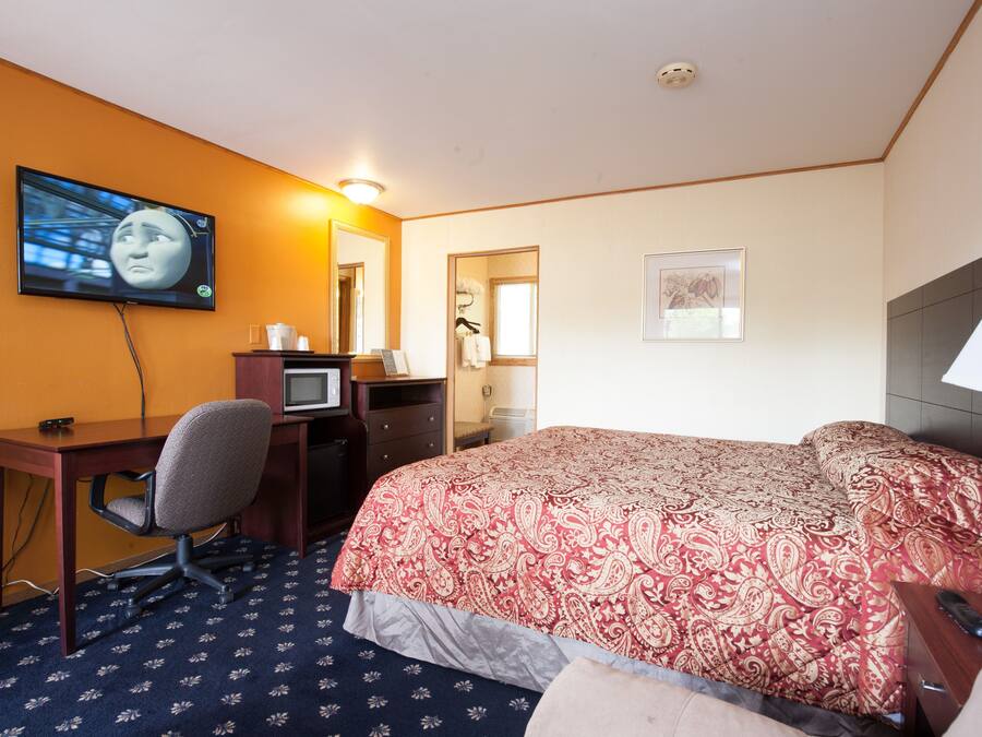 A hotel room with a bed, a desk with a computer, a TV mounted on the wall, and a mirror.