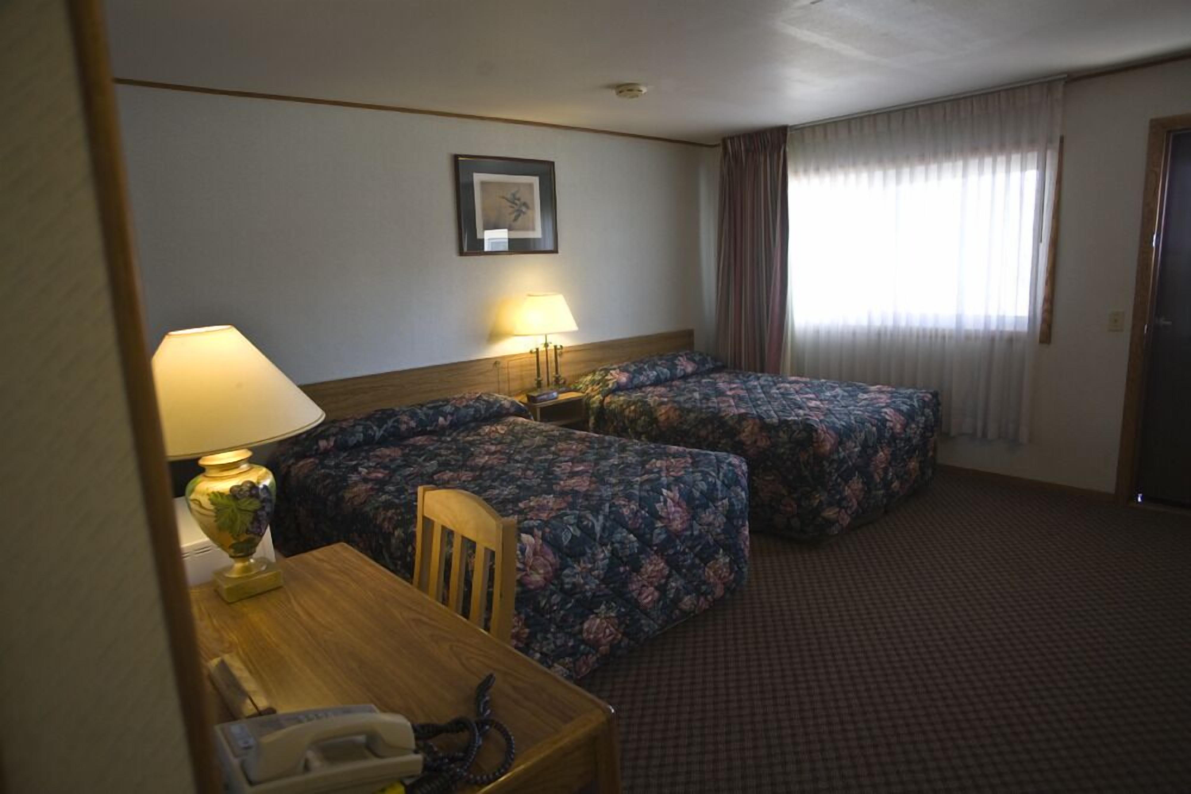 Une chambre d’hôtel avec deux lits, un bureau avec une lampe, un téléphone et un tableau encadré au mur.