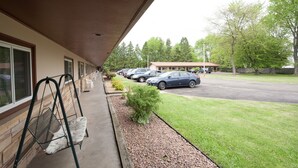 Un hotel con pasarela techada, mesas al aire libre y un estacionamiento lleno de coches.