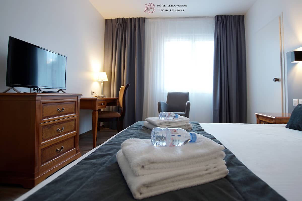 A hotel room with a bed, a desk with a lamp, a chair, a television, and a window with curtains.