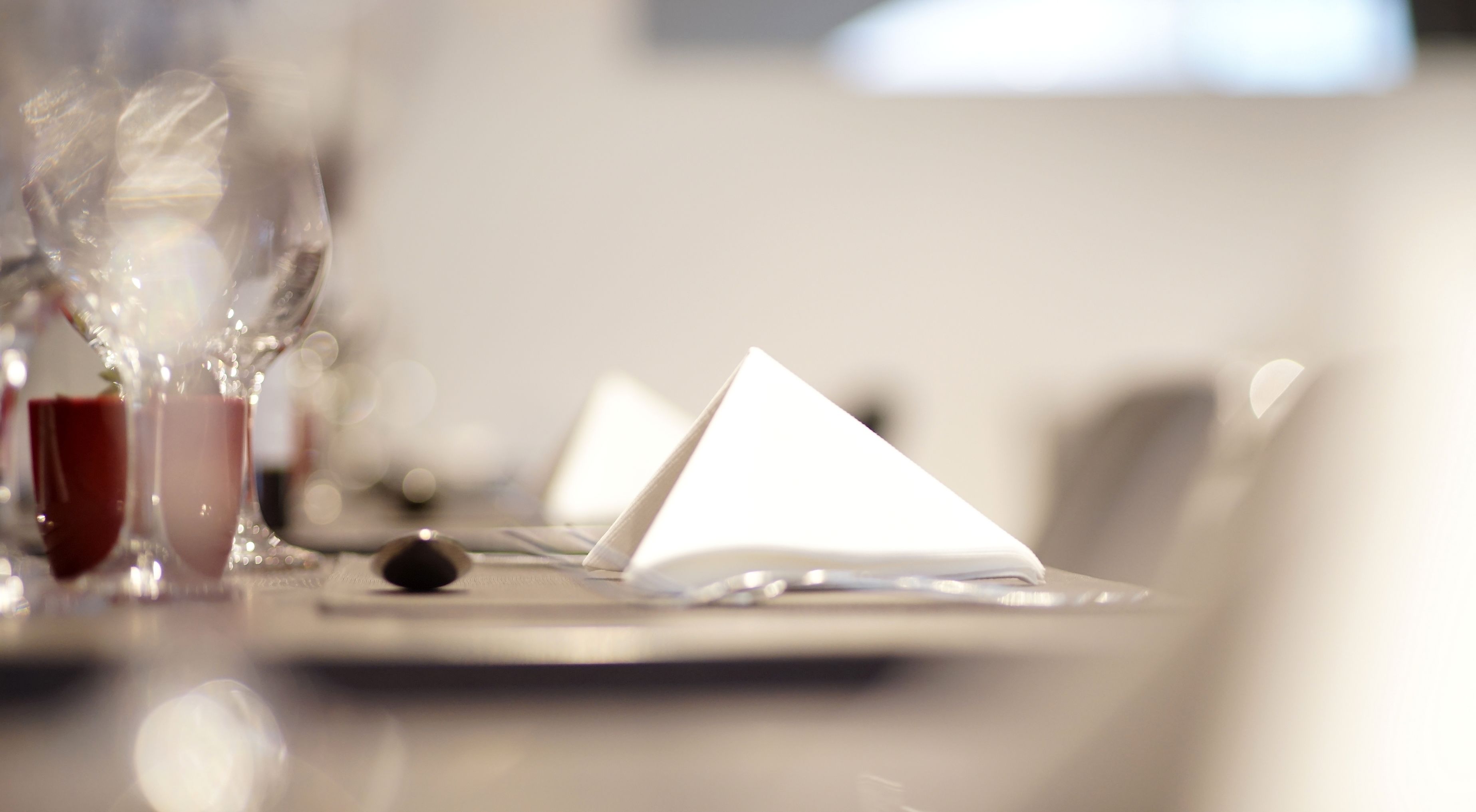 Una mesa de comedor con un mantel blanco doblado con cuidado, una copa de vino tinto y una copa de vino blanco.