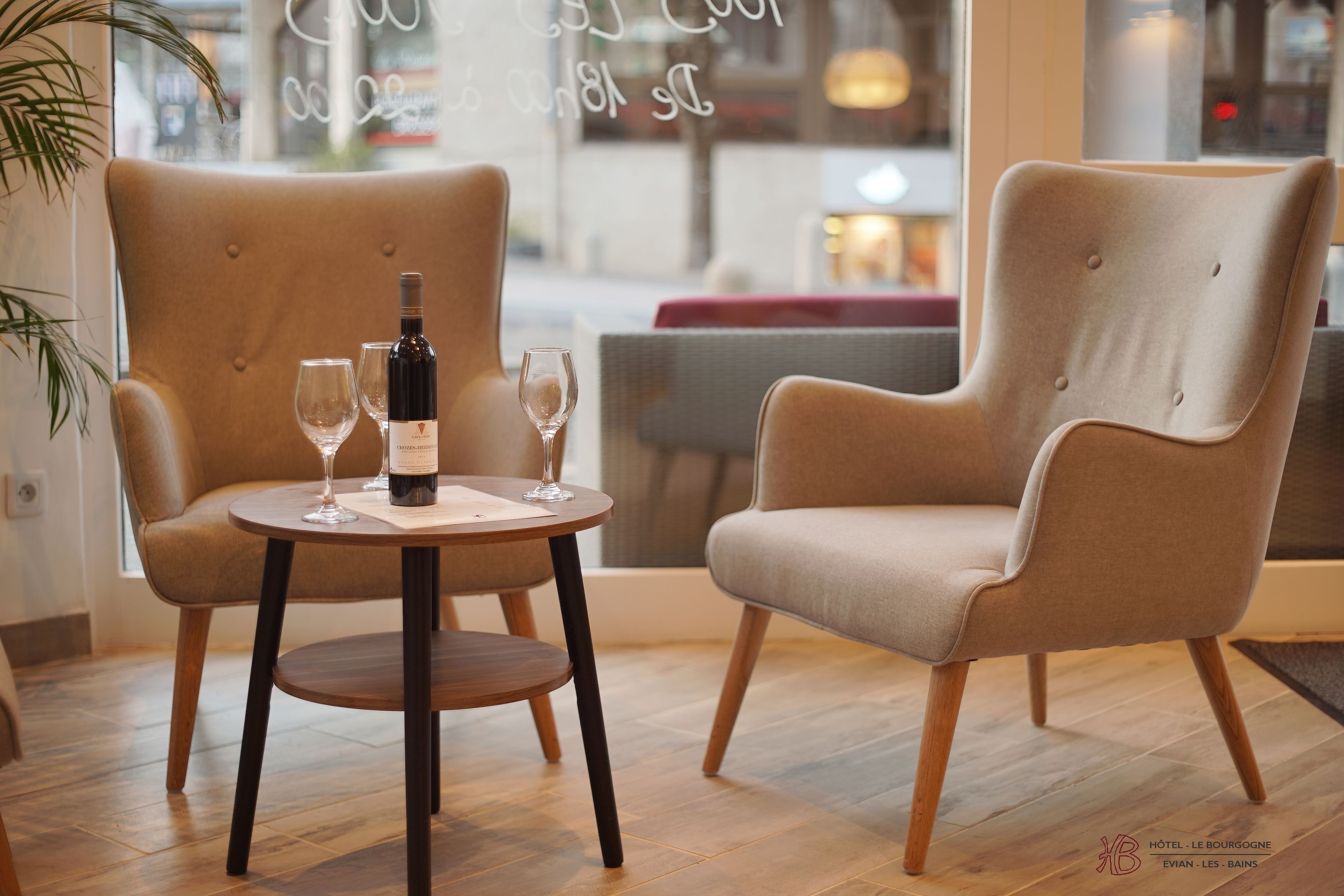 Un interior moderno con dos sillones color beige y una mesa redonda, una botella de vino y dos copas de vino.