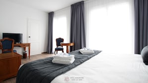 Une chambre d’hôtel avec un lit, un bureau, une chaise, une télévision et une fenêtre avec des rideaux.