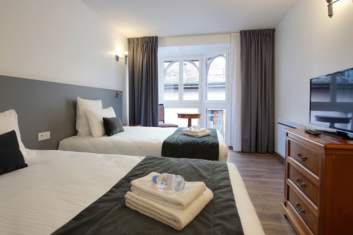 A hotel room with two beds, a TV, a wooden dresser, and a balcony with curtains.