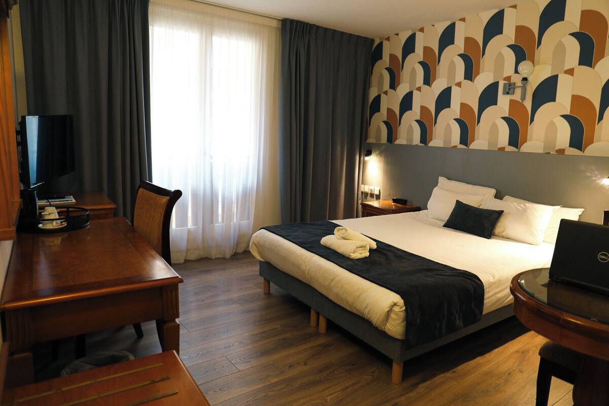 A hotel room with a bed, a desk, a chair, a television, and a laptop.