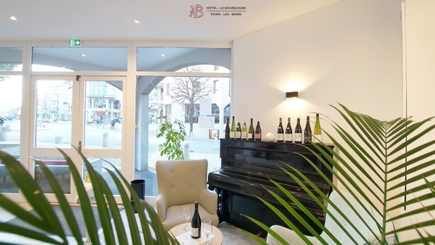 Un hall d’hôtel avec un piano, un coin salon et une présentation de bouteilles de vin.