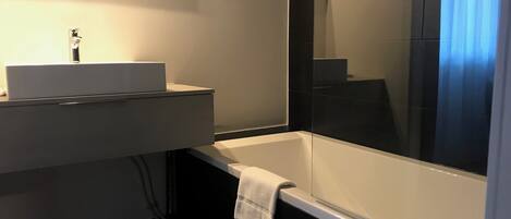 A modern bathroom with a white sink, mirror, and bathtub.