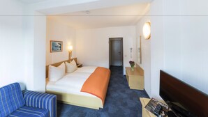 A hotel room with a bed, a blue-striped sofa, a TV, and a bedside table with a lamp and a vase of flowers. - Hansa Hotel (Düsseldorf)