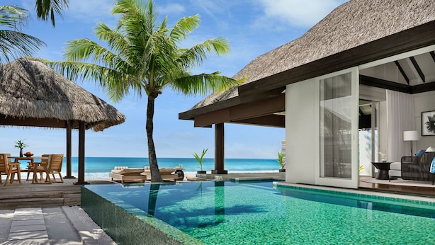 Un resort con piscina, construcciones de techo de paja y vista al océano.
