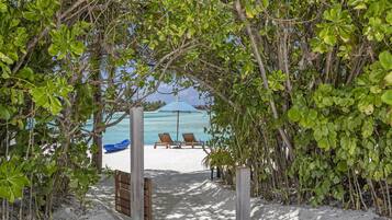 A beach pathway leading to a sandy beach with two lounge chairs and a blue umbrella.