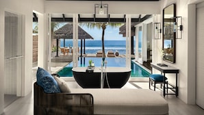 Una piscina infinita moderna con vistas despejadas al océano, un área de estar confortable con un sofá y un sillón, y una habitación bien iluminada con un espejo grande y una mesita.