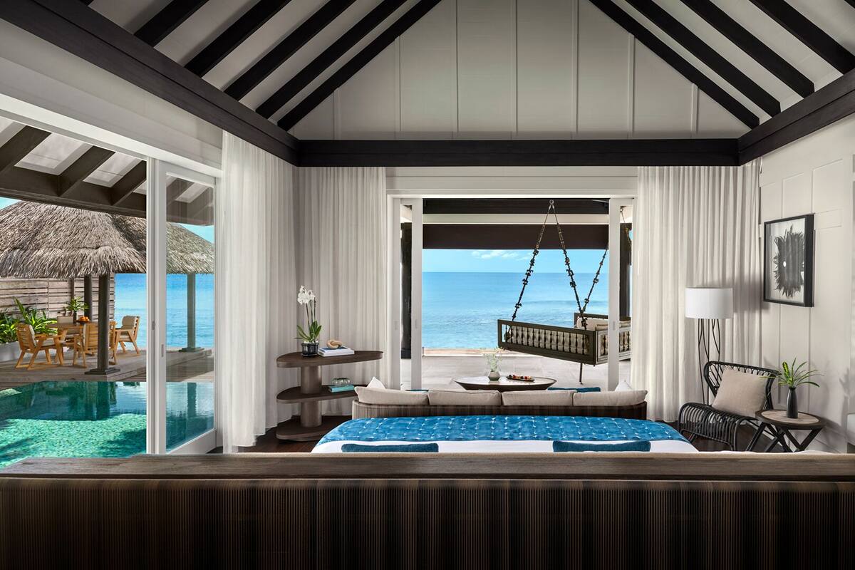 A hotel room with a bed, a hanging chair, a small table, and a view of the ocean.
