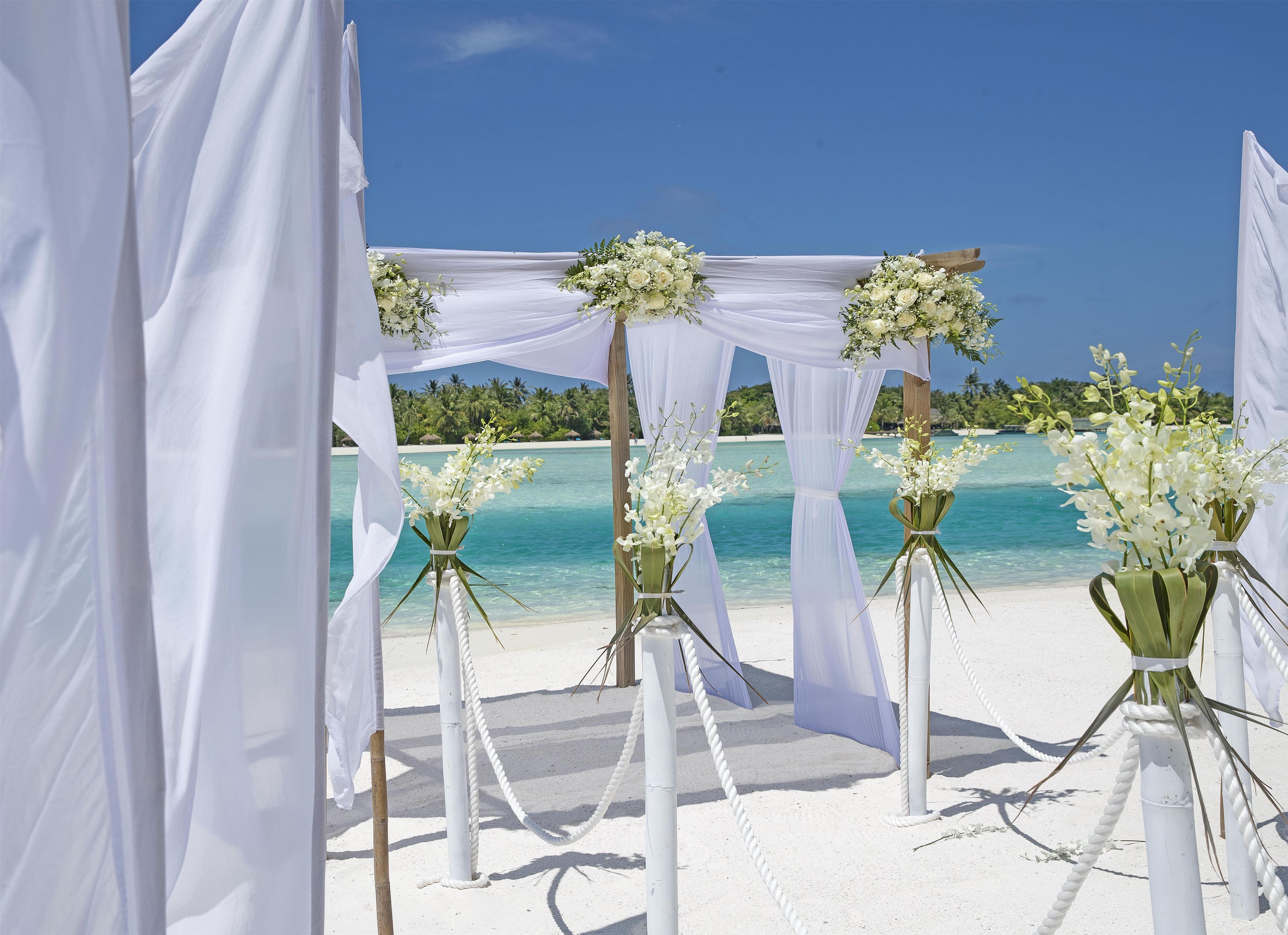 Hochzeitsdekoration am Strand mit weißen Vorhängen und Blumenarrangements.