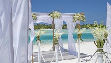 Hochzeitsdekoration am Strand mit weißen Vorhängen und Blumenarrangements.