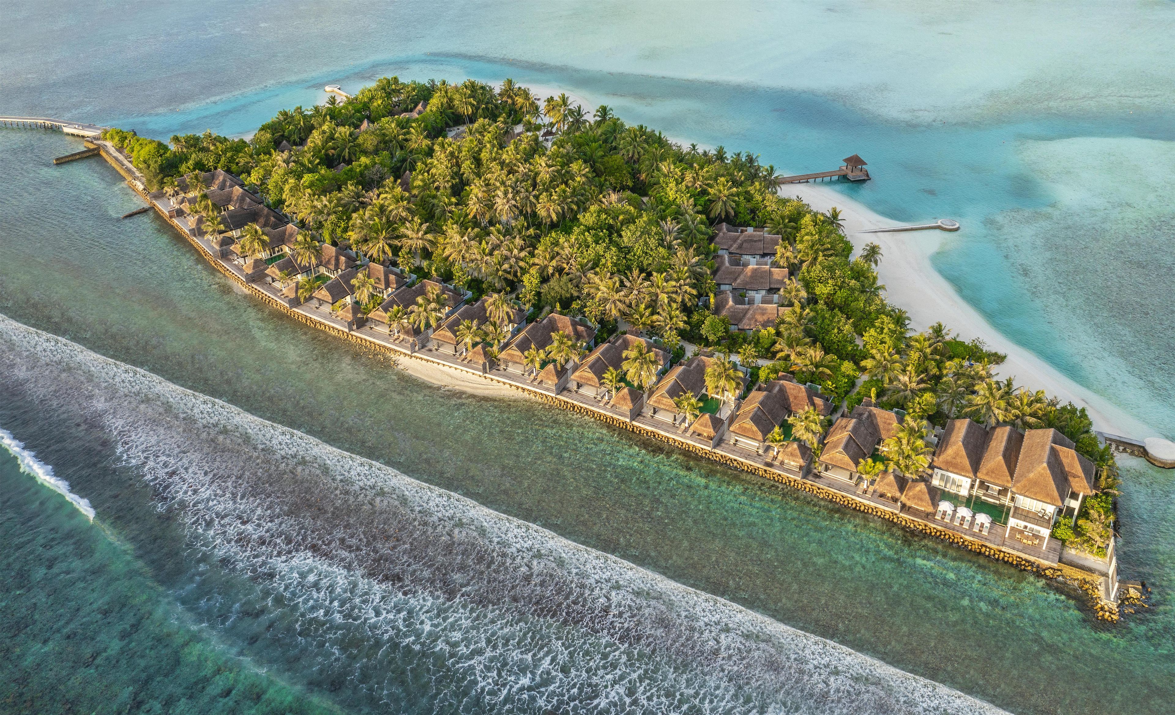 Ein Luftbild eines tropischen Inselresorts mit Bungalows über dem Wasser, einer Anlegestelle und klarem türkisblauem Wasser.
