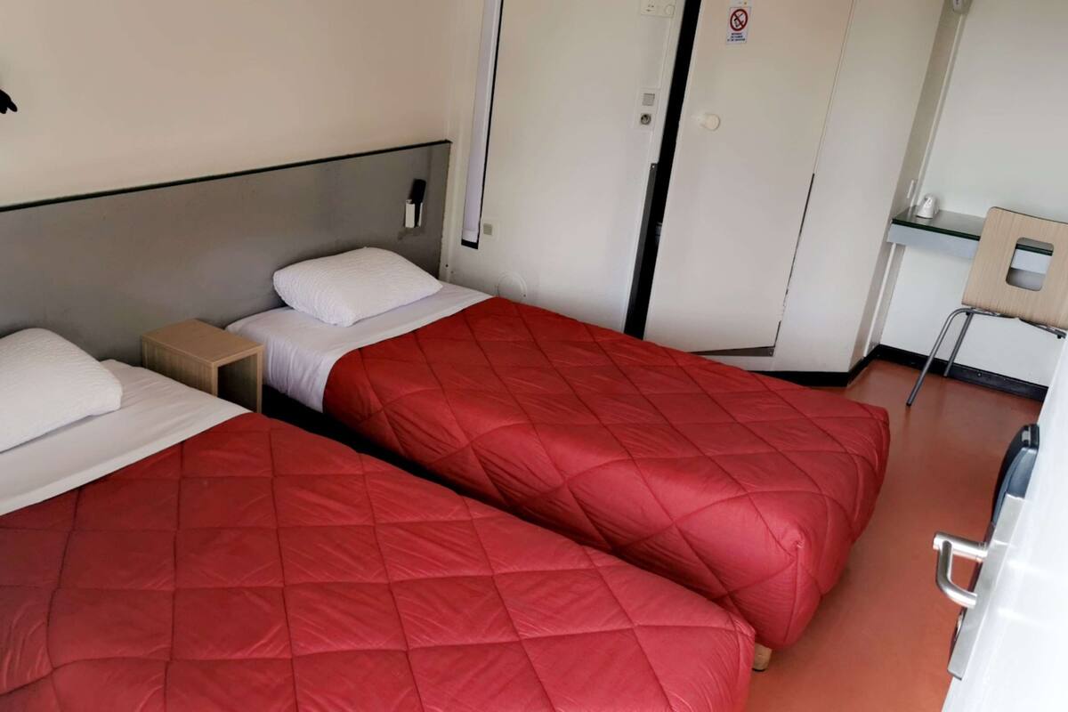 Een hotelkamer met twee bedden, een tafeltje, een stoel en een kledingkast.