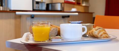 Bandeja de desayuno con jugo de naranja, croissant y una taza sobre una mesa en una habitación de hotel.