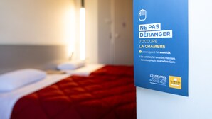 Une chambre d’hôtel avec un lit, une lampe de chevet et un panneau avec du texte en français.