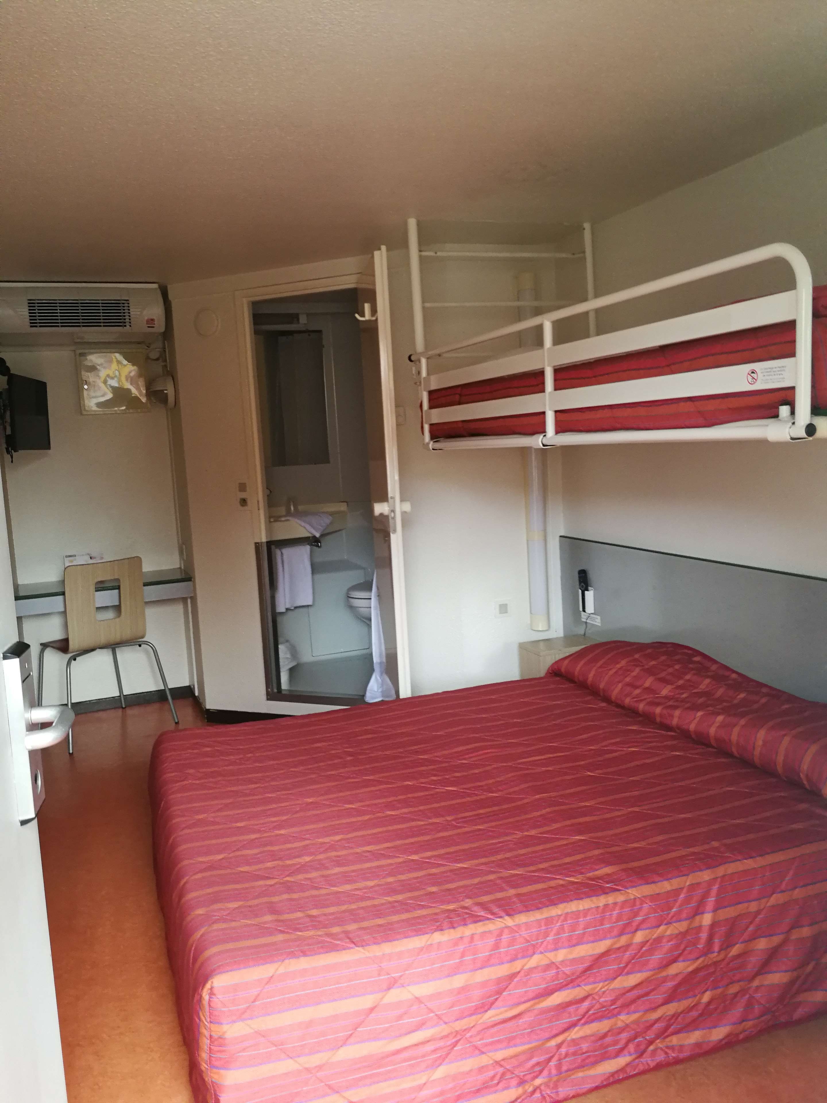 A compact room with a bunk bed, a desk with a chair, a mirror, and a window.