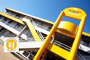 Un hôtel à la façade jaune, doté d’un escalier et d’une enseigne indiquant « HÔTELS DE PREMIÈRE CLASSE ».