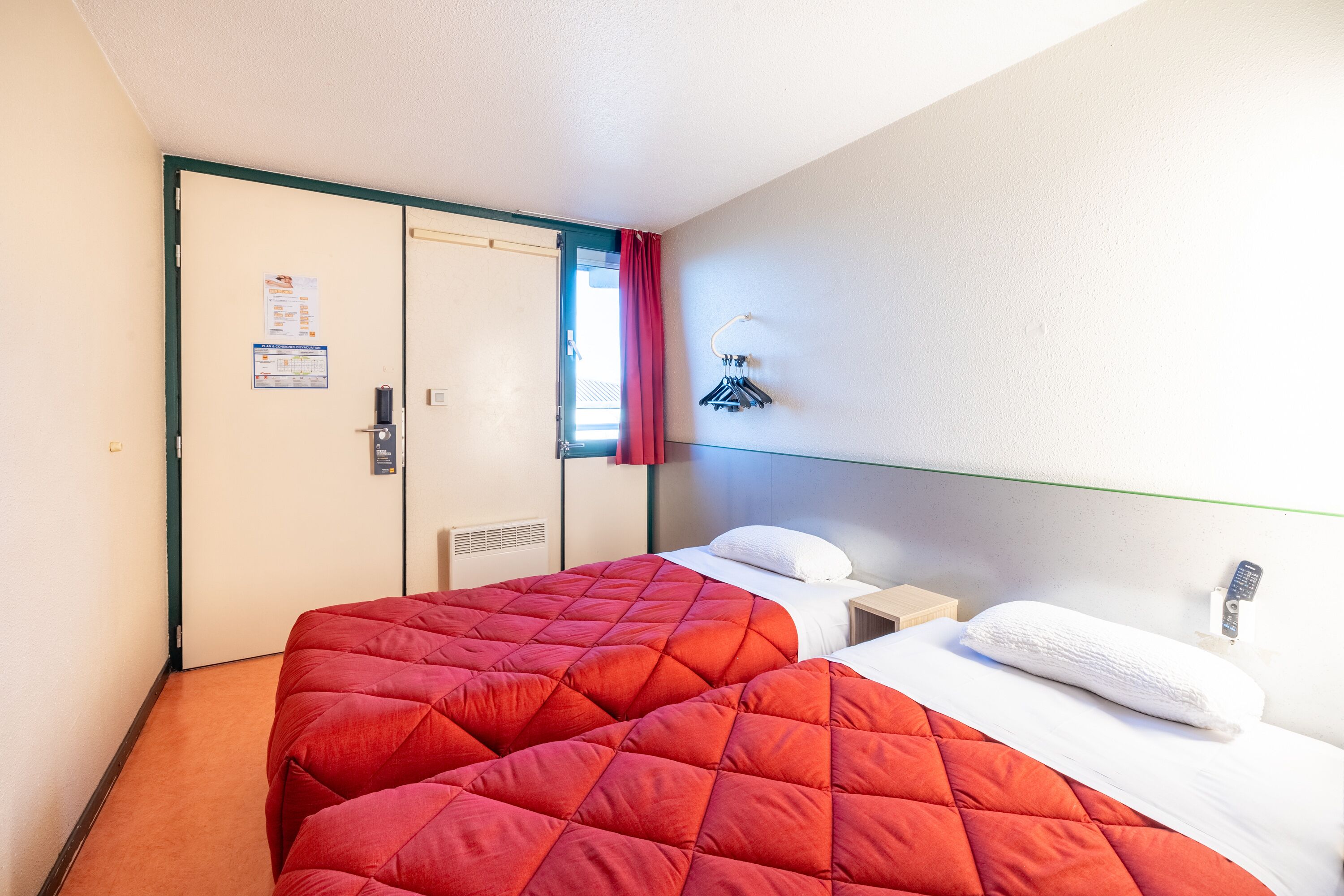 A hotel room with two beds, a wardrobe, a nightstand, and a wall-mounted towel rack.