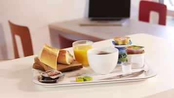 A breakfast tray with toast, juice, coffee, yogurt, and a newspaper on a hotel table.
