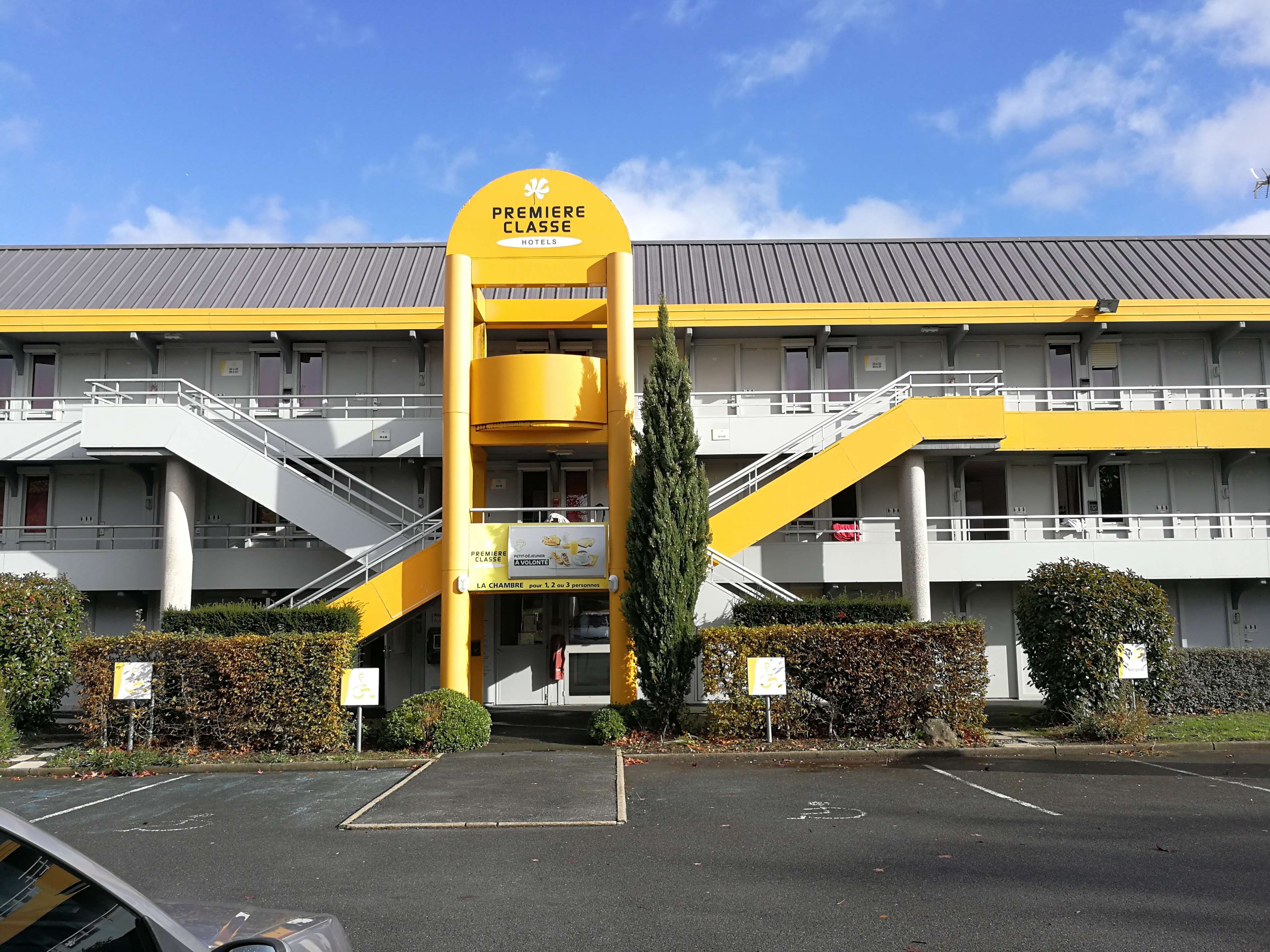 Un hotel con una decoración en amarillo y blanco, que cuenta con una entrada destacada con una escalera y un cartel que indica que es un hotel 'Première Classe'.