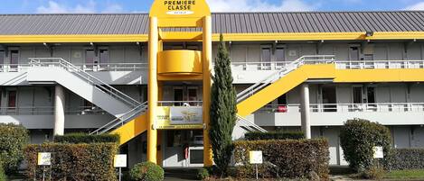 Un hotel con una decoración en amarillo y blanco, que cuenta con una entrada destacada con una escalera y un cartel que indica que es un hotel 'Première Classe'.
