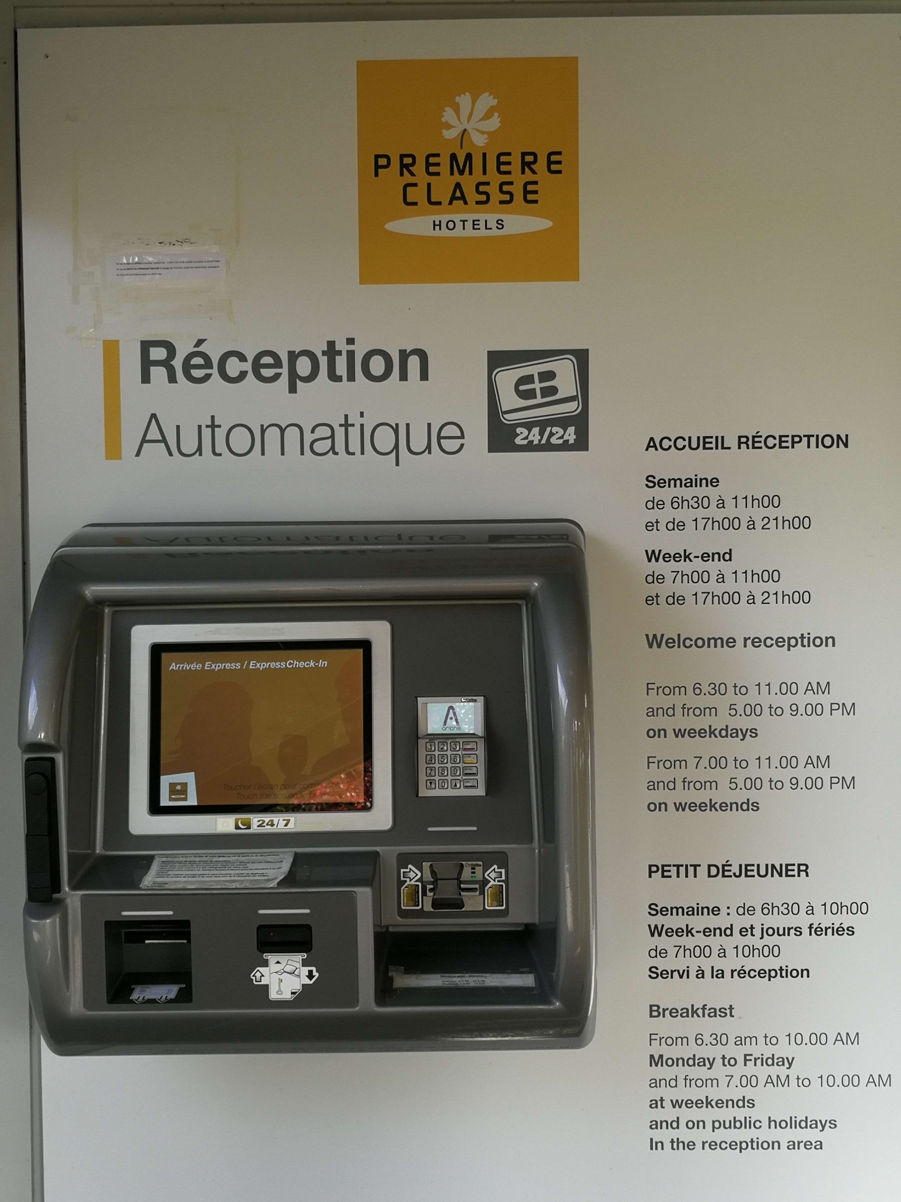 Una máquina de recepción automatizada con pantalla, teclado y lector de tarjetas, y un cartel con el nombre del hotel y el horario de recepción.
