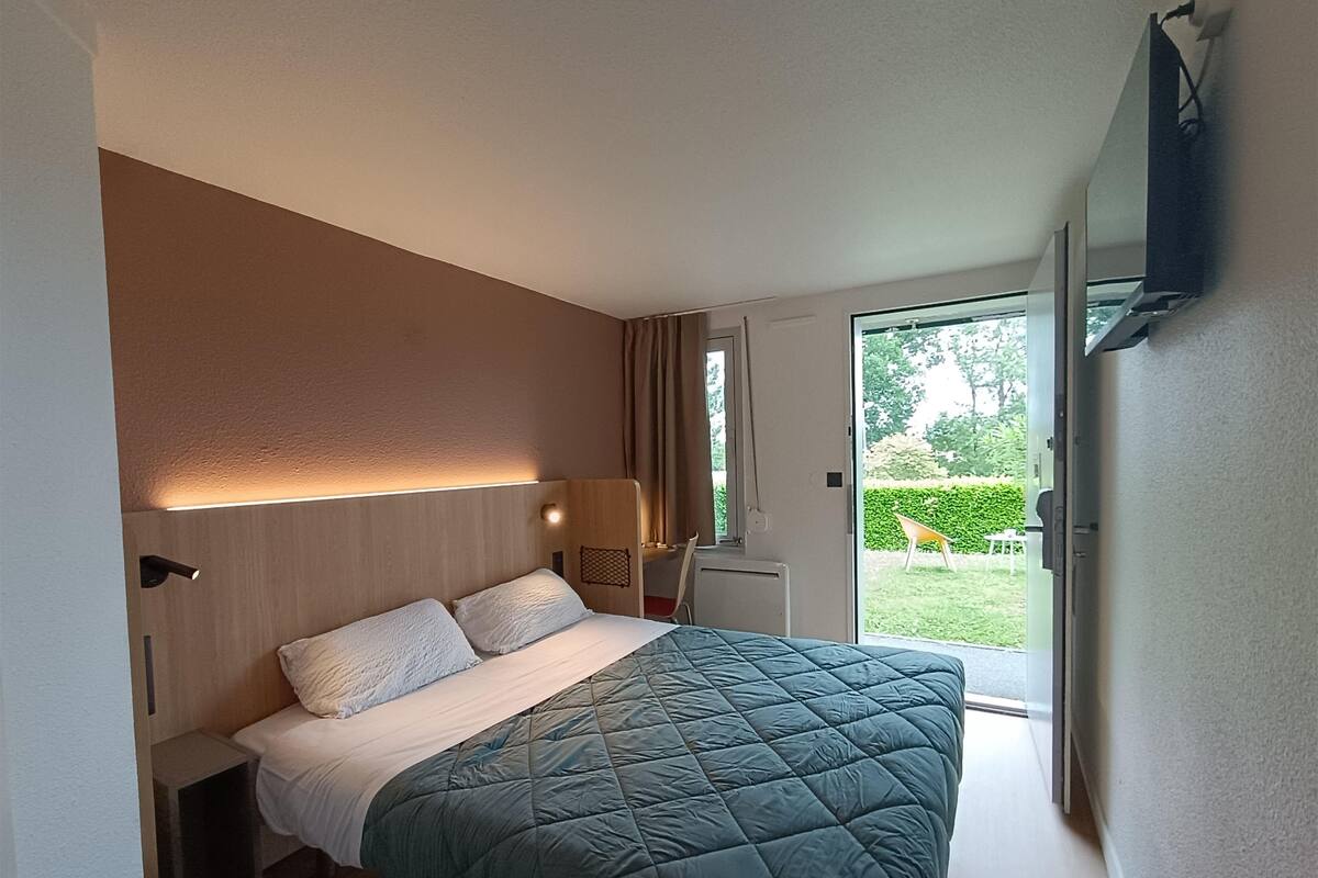 Un dormitorio con cama, mesita de noche, lámpara y vistas al exterior.