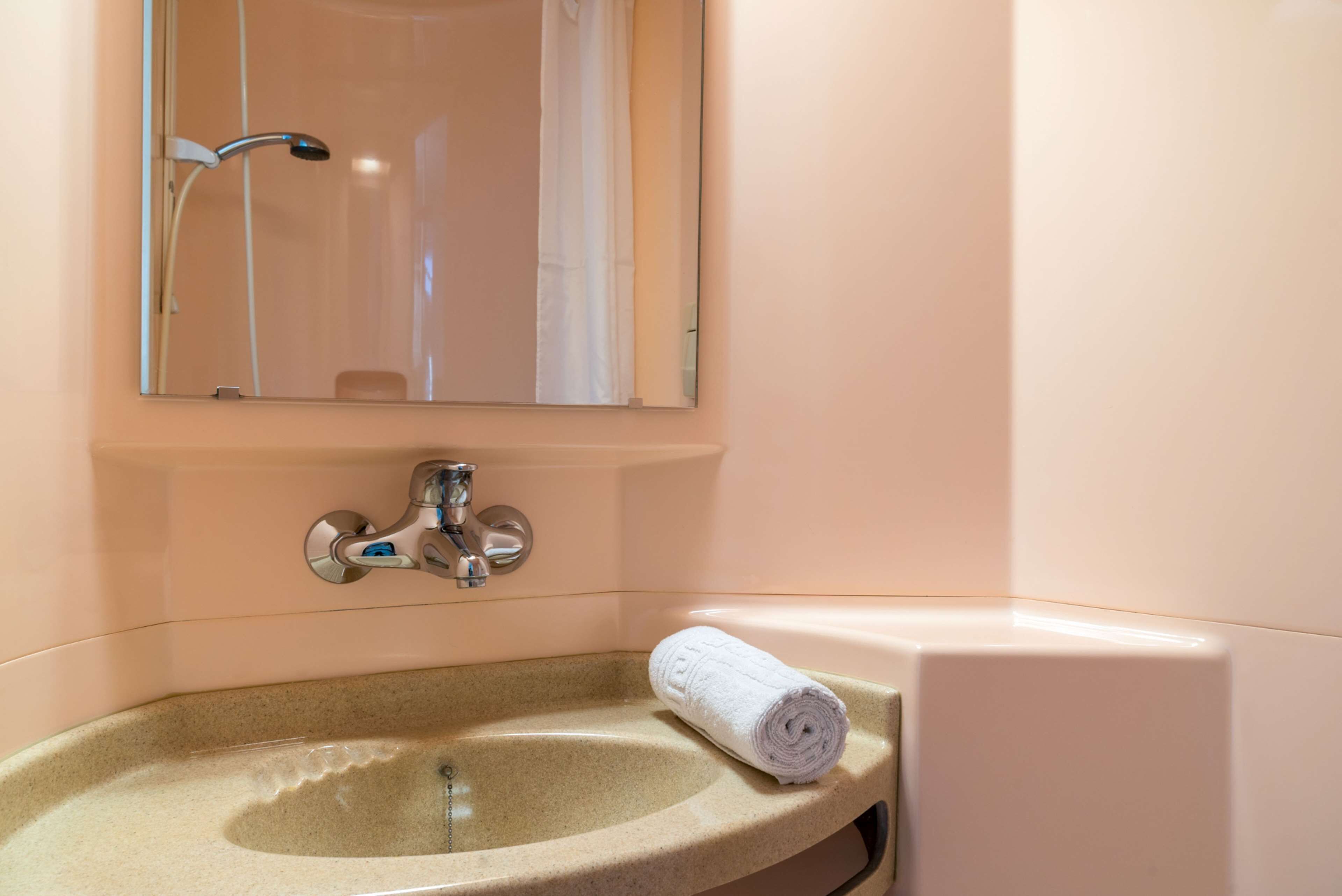A bathroom with a beige sink, a mirror, and a towel.