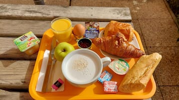 Una bandeja con alimentos para el desayuno, incluyendo un croissant, una manzana, zumo de naranja y una taza de café.
