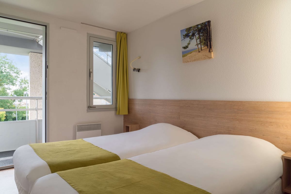 Habitación de hotel con dos camas, una ventana con cortina, un cuadro colgado en la pared y una mesita de noche.