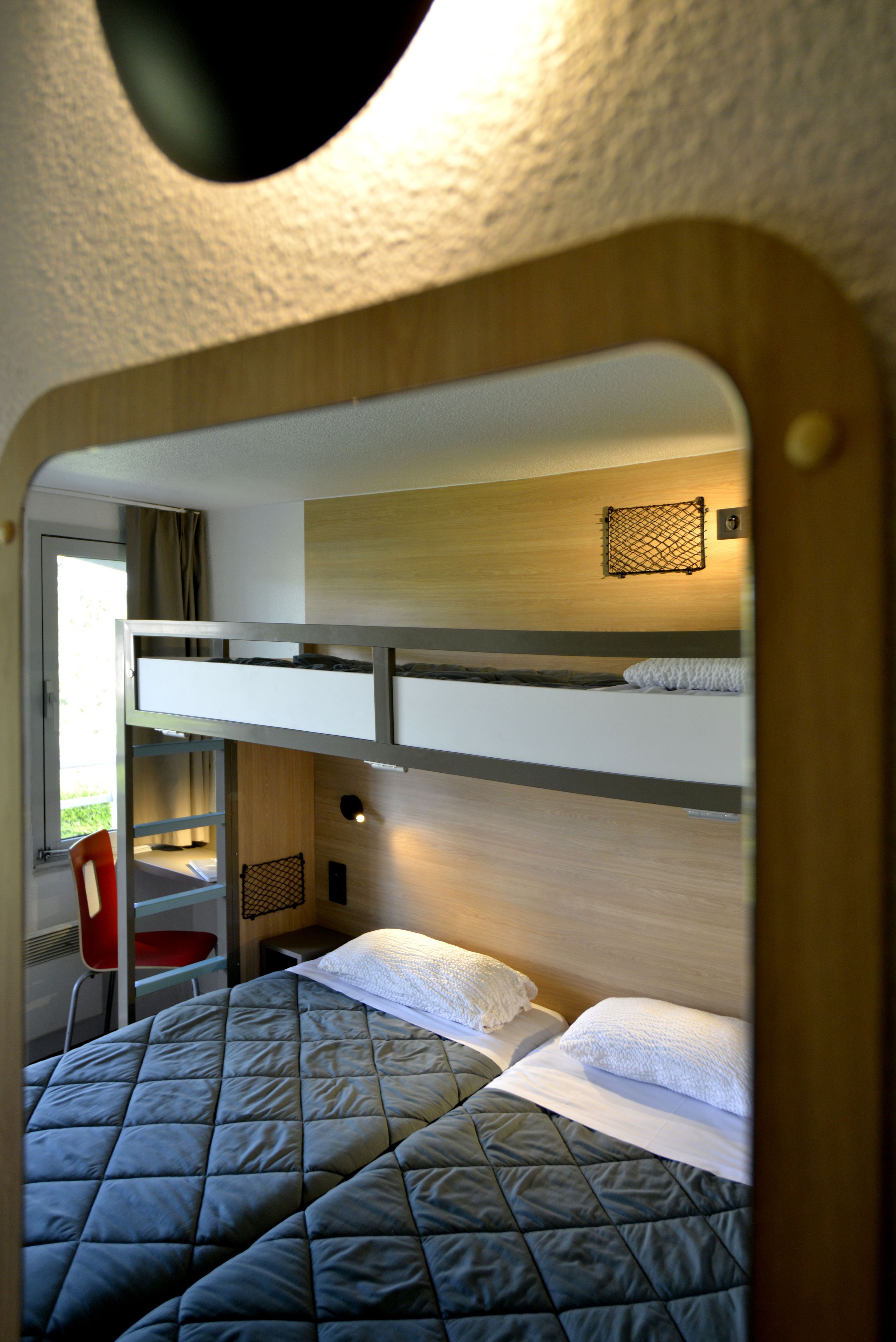 Habitación con literas, un escritorio, una silla, una ventana con cortinas y una lámpara fijada a la pared.