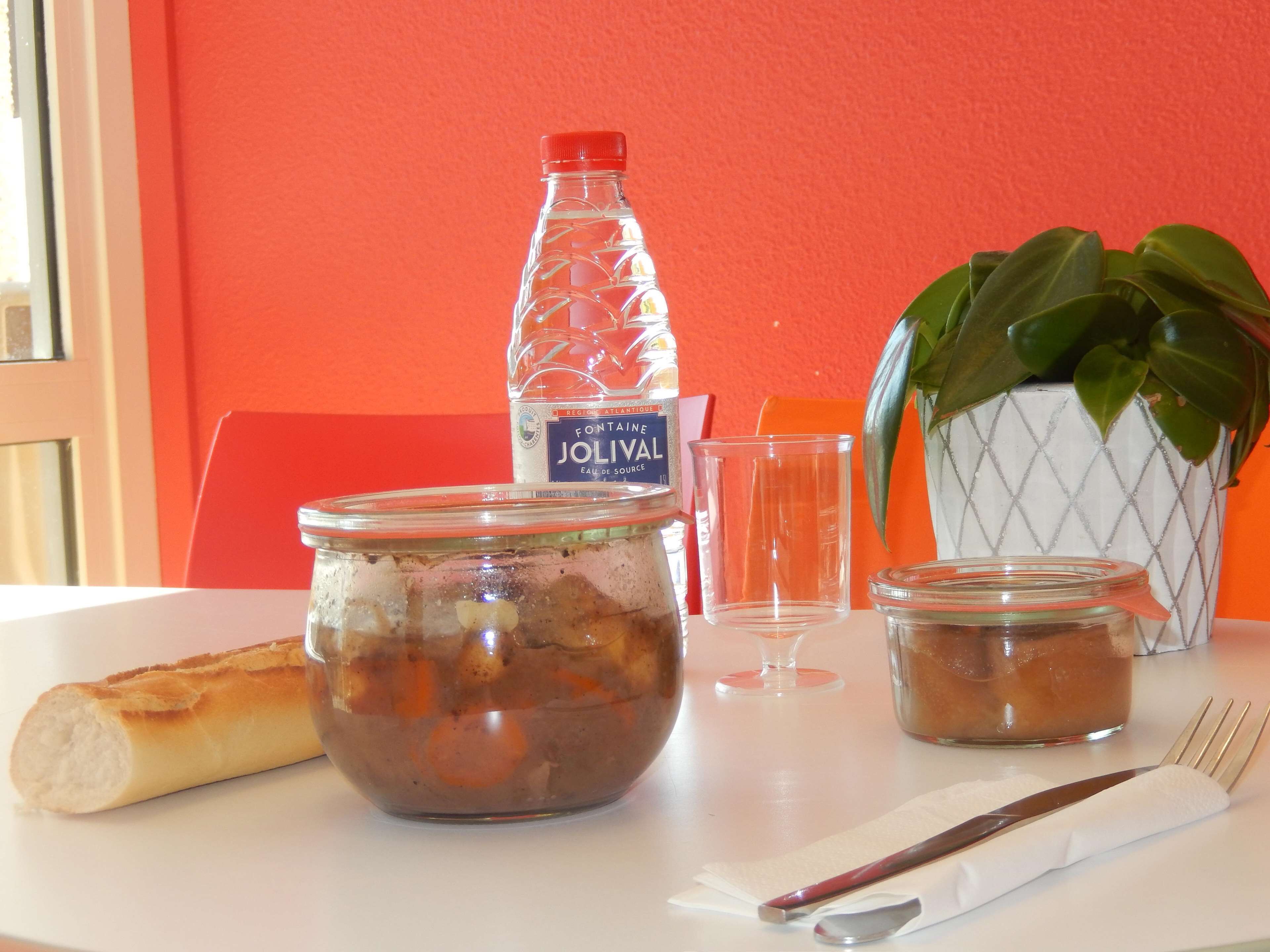 Ein Tisch mit einer Vorratsglocke, einer Wasserflasche, einem Glas, einer Pflanze und einem Baguette.