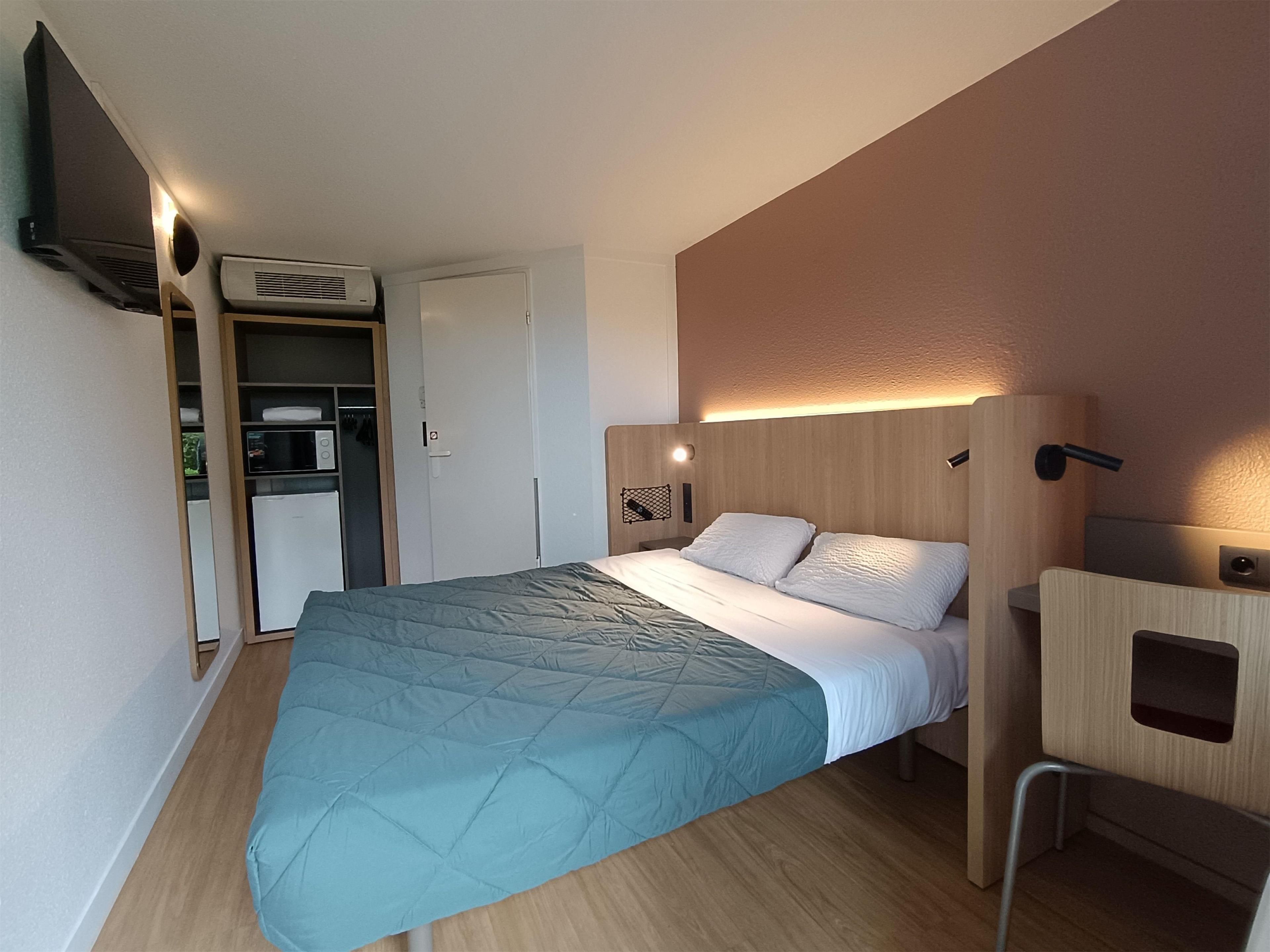 Una habitación de hotel moderna con una cama, un escritorio, un armario y un televisor.