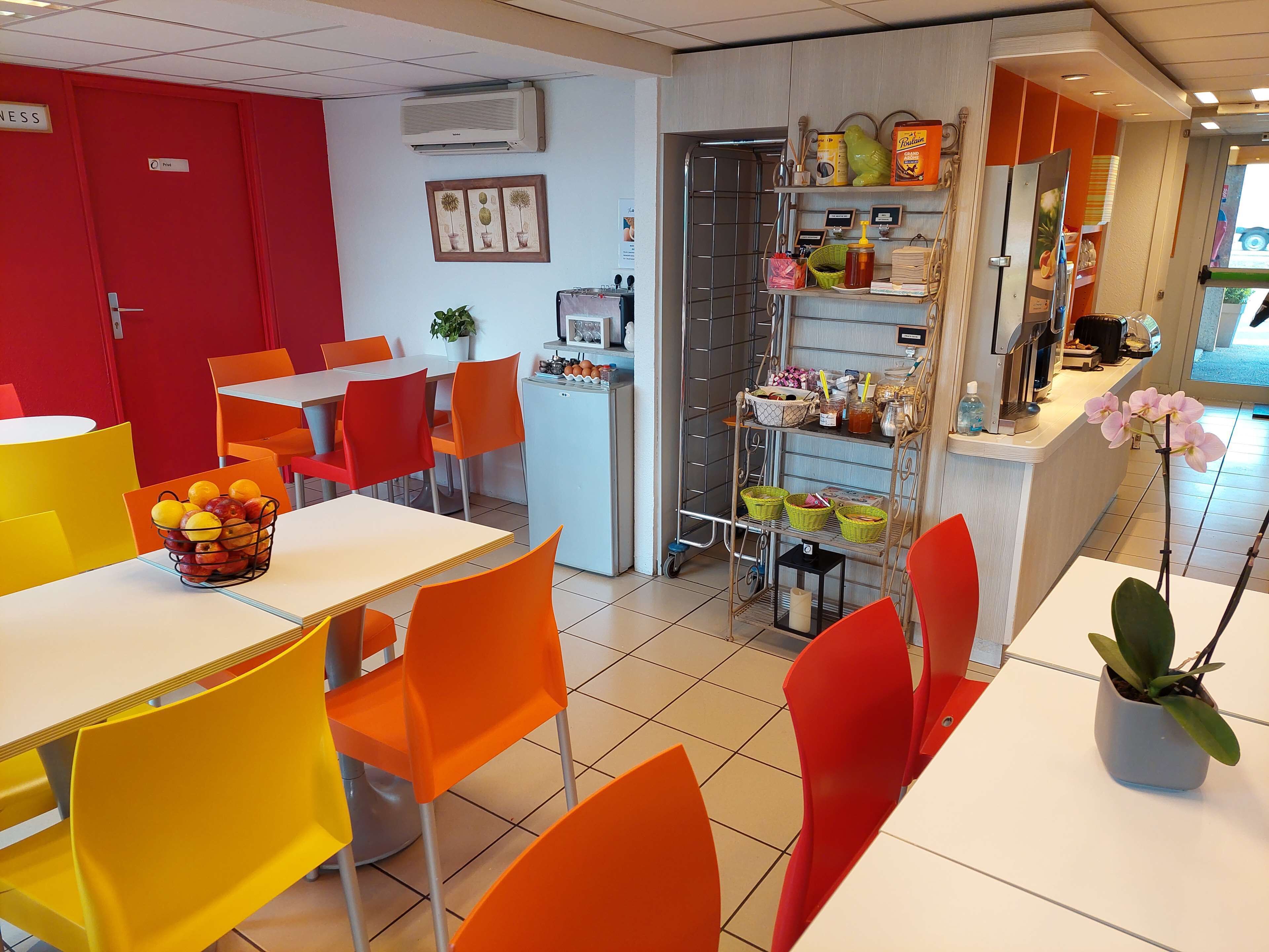 Ein hell erleuchteter Essbereich mit orangefarbenen Stühlen und Tischen, einem kleinen Kühlschrank und einer Theke mit verschiedenen Gegenständen.