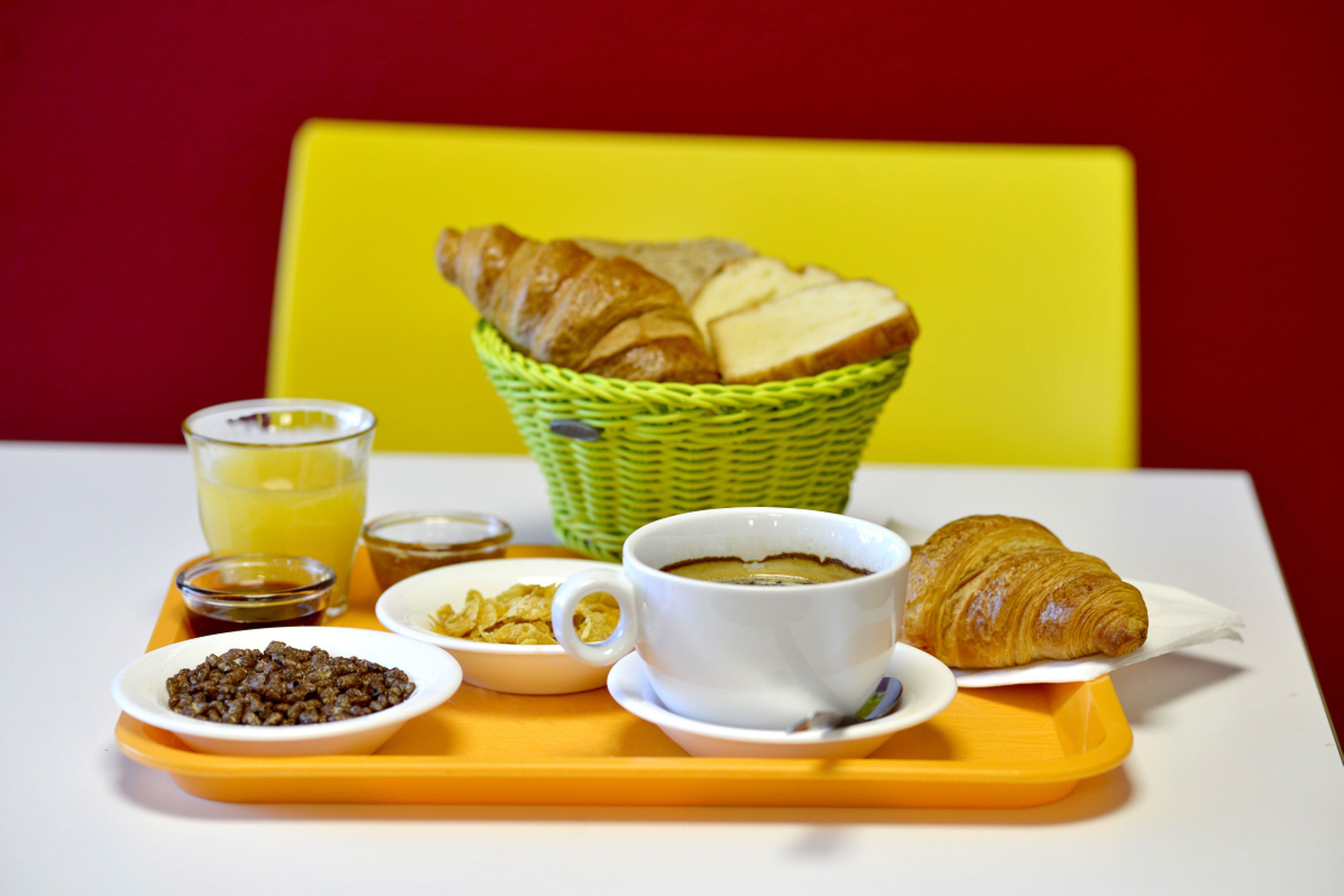 A breakfast tray with croissants, a cup of coffee, cereal, and a glass of juice.
