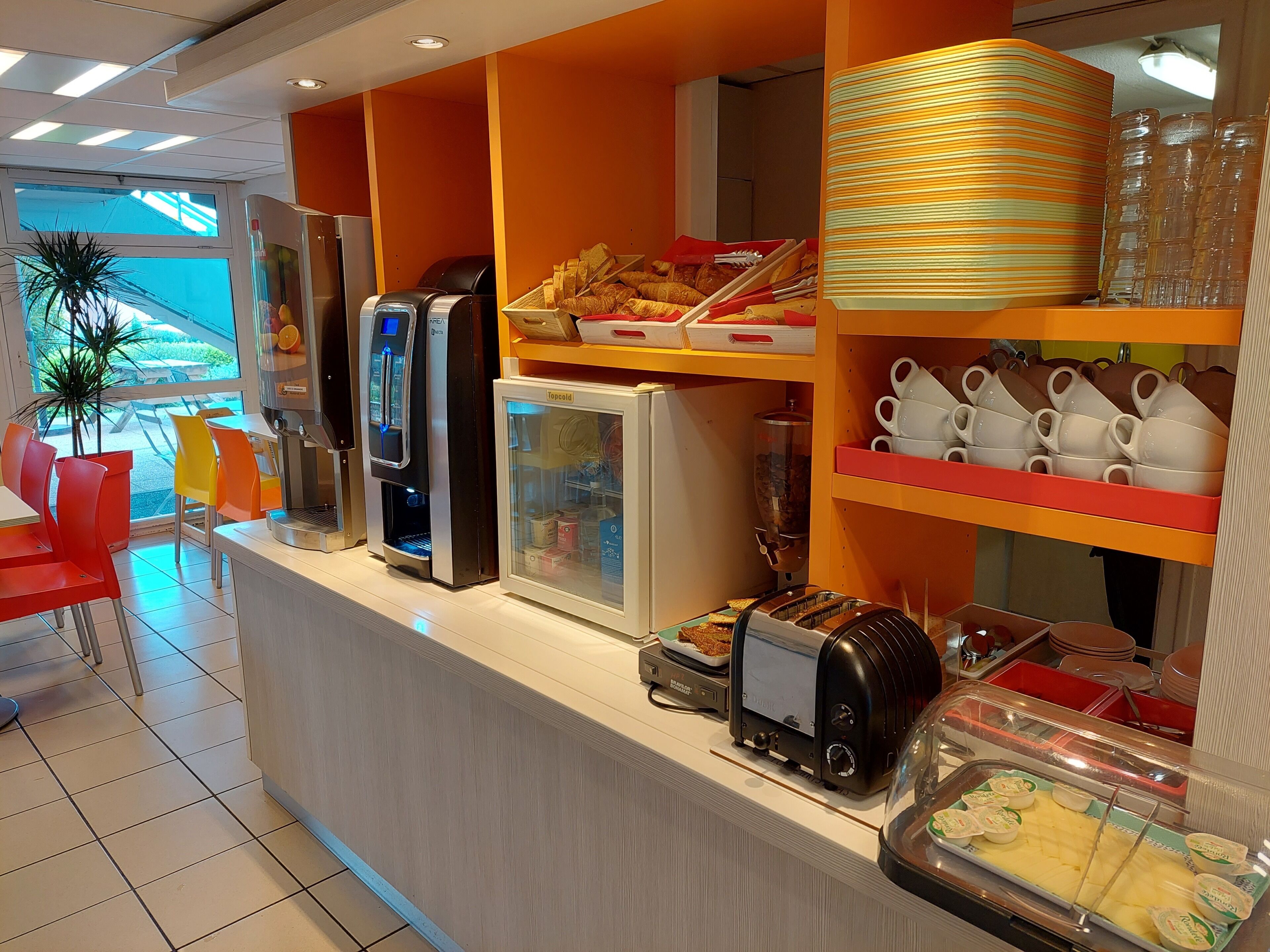 A breakfast bar with various food items, a coffee machine, a toaster, and a refrigerator.